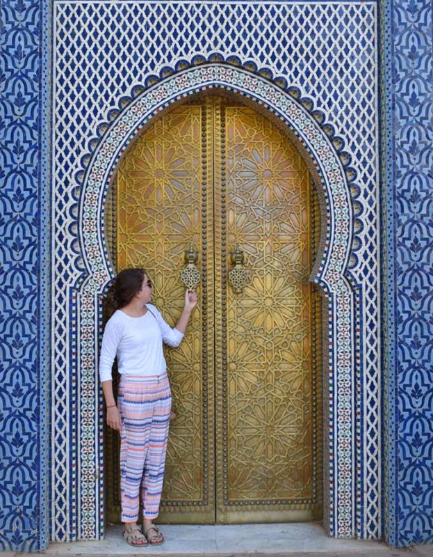 Sarah Proper standing in front of a gold door encased in a Moroccan blue tile